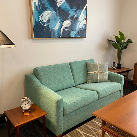 Green sofa in a living room with a painting on the wall and decorative items on tables. This is the macquarie range by Parker Furniture, reupholstery carried by Covesmore. Ex Parker People™