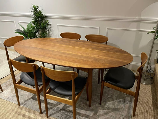 A Mid Century dining table with chairs in a room with plants and a rug. This table is available for sale in Sydney.