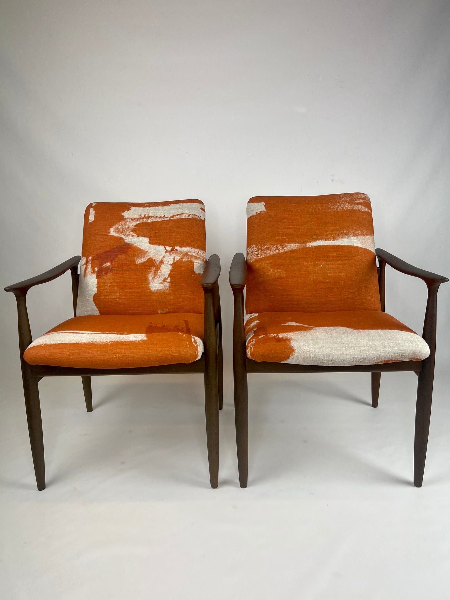 A pair of Parker 119 dining chairs with orange and white upholstered padded backrests and seats, featuring floating armrests on a polished wooden frame. Available online for sale.