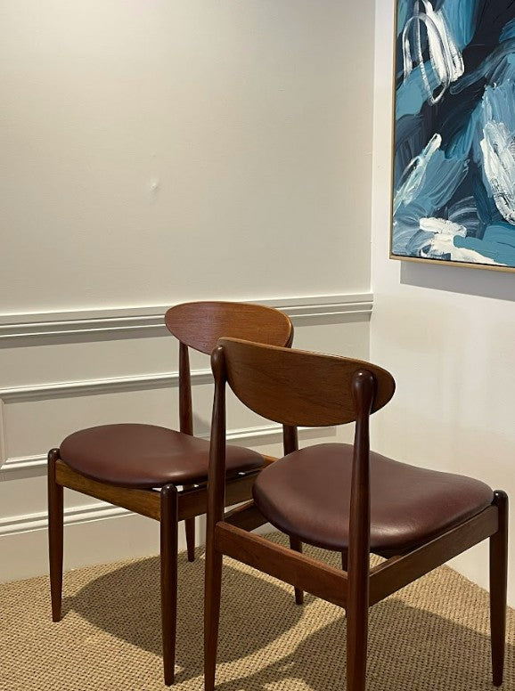 Two wooden Parker chairs with brown leather seats in a room with a painting on the wall. Parker 107 chairs, available for sale in Sydney.