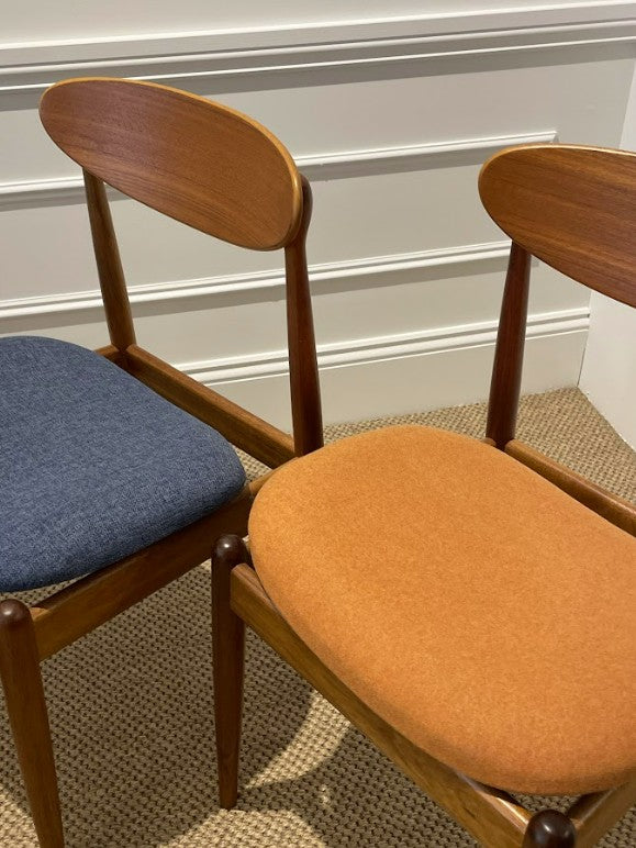 Two wooden Parker 107 dining chairs with fabric seats, one blue and one orange, against a neutral wall. Available for Sale at Willoughby.