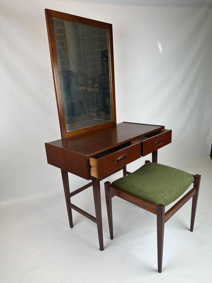 A vintage Parker dresser with a stool in front of it. The dresser has a mirror on top and two drawers, with the stool having a green cushion.