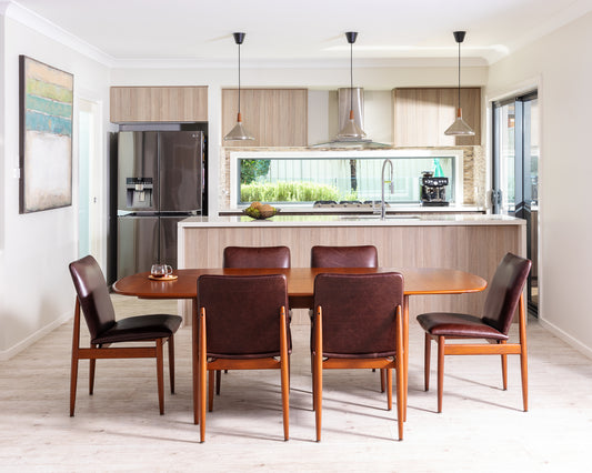 A set of Parker dining chairs with brown leather upholstery and wooden legs, around a Parker dining table in a modern kitchen setting. Parker Furniture For Sale In Willoughby.