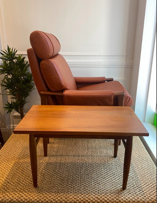 Brown leather Tessa chair with a wooden mid-century table in a room with a plant and light-colored walls. Ex Parker People™