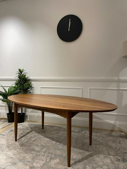 A Mid Century wooden dining table in a room with a clock on the wall and plants. Available for sale in Willoughby.