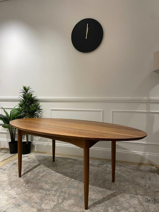 A Mid Century wooden dining table in a room with a clock on the wall and plants. Available for sale in Willoughby.