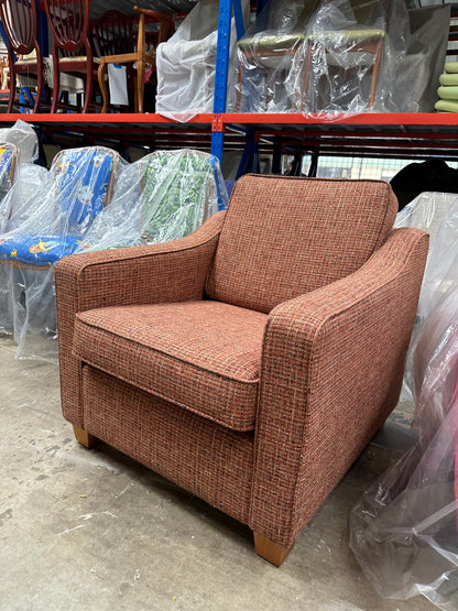 This armchair is part of the Macquarie range by Parker furniture. Brown upholstered chair in a storage or warehouse setting with plastic-wrapped items in the background.