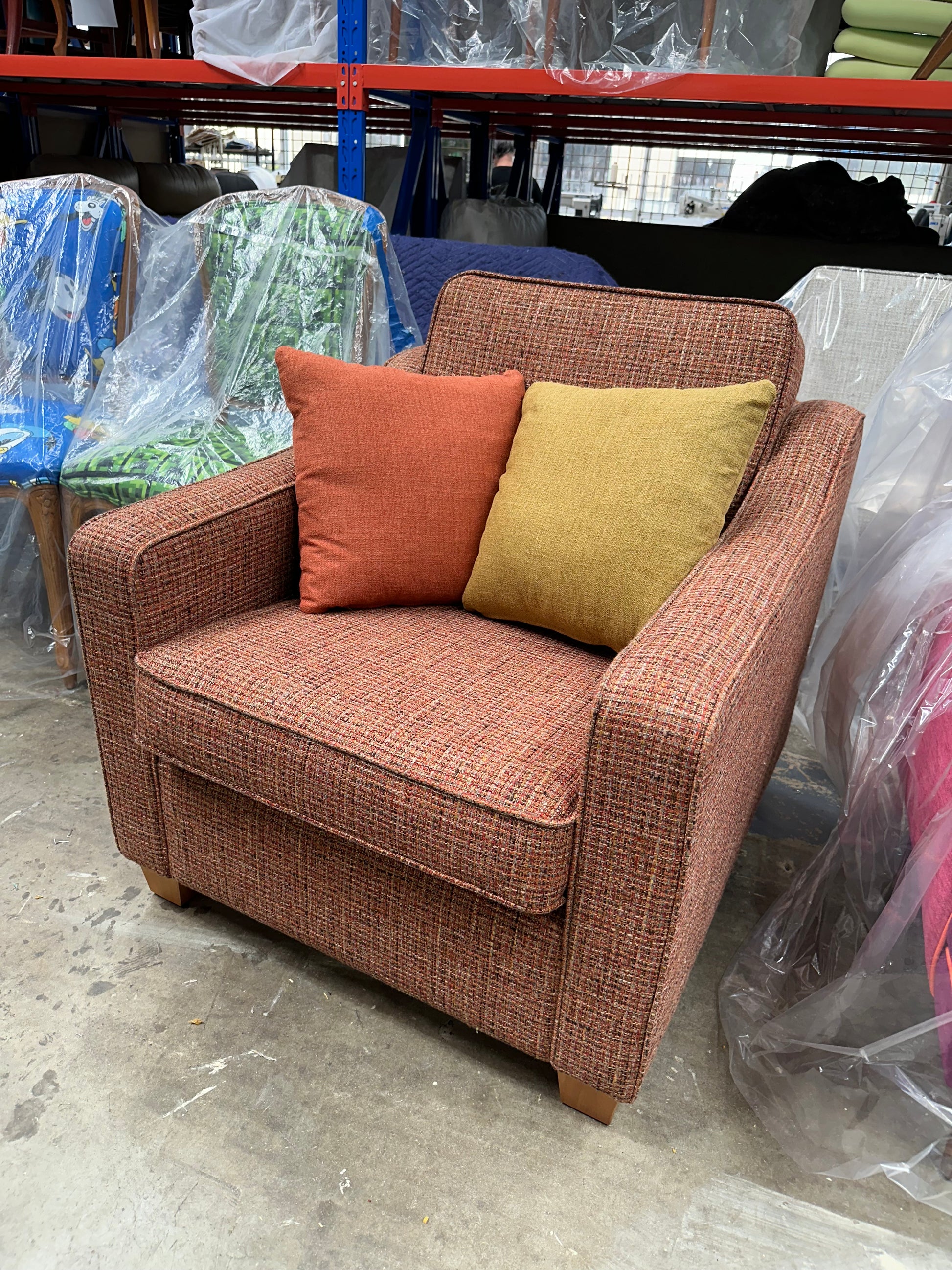Brown sofa with colorful cushions on a concrete floor, surrounded by plastic and other furniture. This armchair is part of the Macquarie range by Parker furniture. Fully restored by Covesmore Solutions.