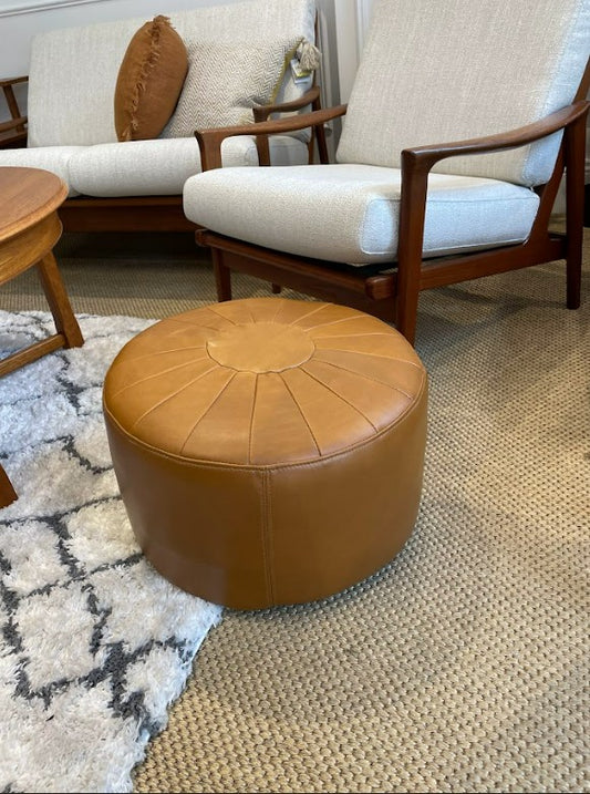Brown leather ottoman in front of a beige armchair on a textured rug. Available in Willoughby showroom. Ex Parker People™